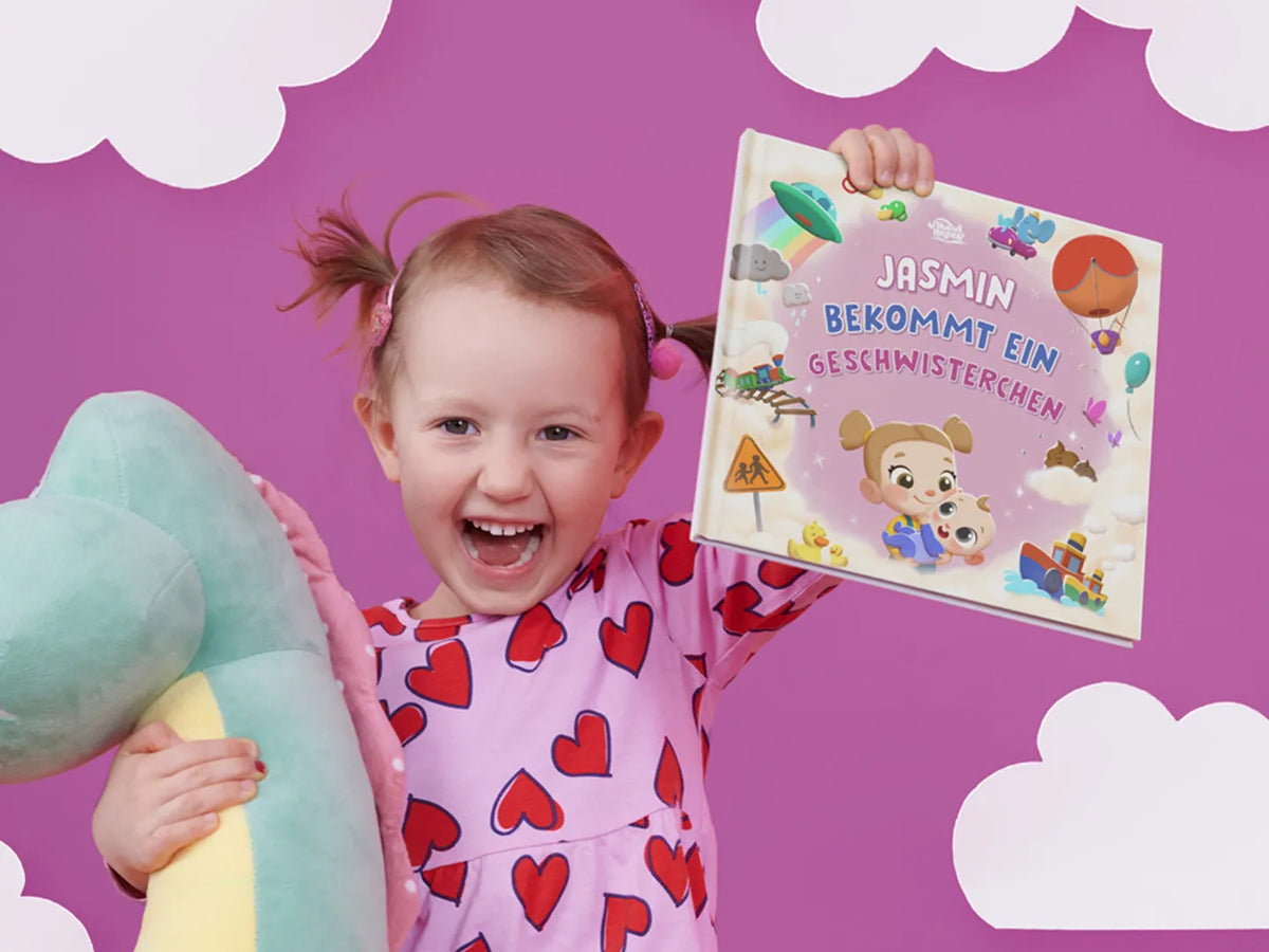 Glückliches Mädchen hält stolz ihr personalisiertes Geschenk, ein Buch darüber, wie man eine große Schwester wird, nachdem sie ihren kleinen Bruder begrüßt hat.		