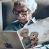 Ein Opa liest im Sessel sein personalisiertes Buch für Großväter und Enkelkinder von Hurra Helden. 