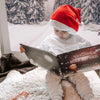 Ein Kind mit Weihnachtsmütze liest sein persönliches Buch, das schönste Geschenk zu Weihnachten.  