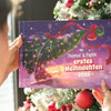 Person hält das personalisierte Weihnachtsbuch „Thomas & Paps – Erstes Weihnachten 2025“ vor einem geschmückten Baum.